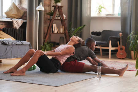 Horizontal full shot of beautiful young woman sitting on floor leaning on to her boyfriends back...