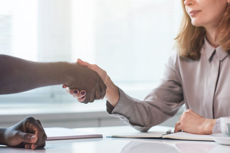 Unrecognizable African American man sitting at table with HR specialist shaking hands with her after...