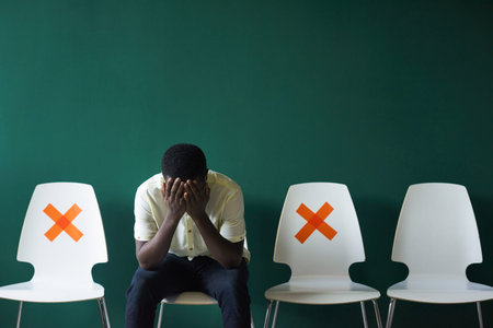 Modern African American man sitting on chair covering his face with hands feeling stressed out after...