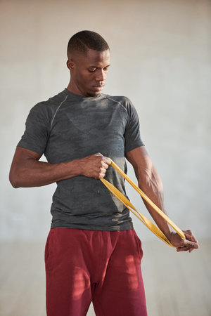 Vertical medium shot of handsome young Black man doing strengthening exercise with resistance band