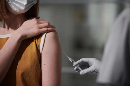 Close-up shot of unrecognizable woman wearing protective mask sitting in doctors office getting vaccine into armの写真素材