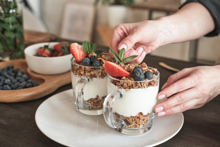 Close-up of unrecognizable woman adjusting leaf while decorating granola with berries in kitchenの写真素材