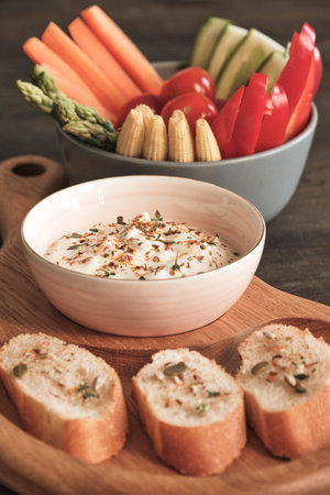 Close-up of appetizers such as vegetable slices and bread toasts with spices on wooden table with white sauceの写真素材