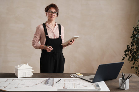 Portrait of content Caucasian interior designer in bodysuit standing with tablet and thinking of new...