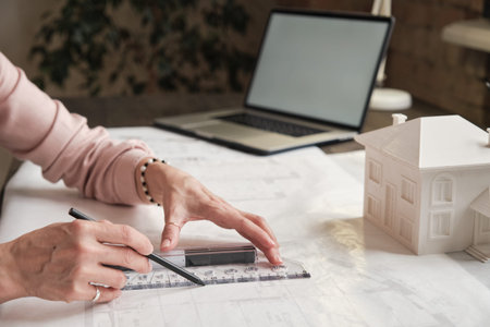 Close-up of unrecognizable female architectural drafter in ring using ruler while working with...