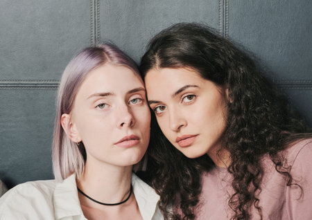 Portrait of serious beautiful homosexual couple of girls touching foreheads against leather...