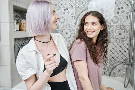 Happy young Caucasian lesbians in homewear laughing while enjoying morning routine togetherの写真素材