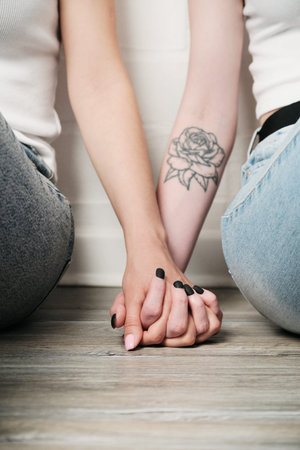 Close-up of woman with rose tattoo holding hand of girlfriend on floor