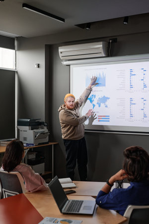 Portly young Caucasian marketing specialist presenting survey data after analysis to colleagues in...