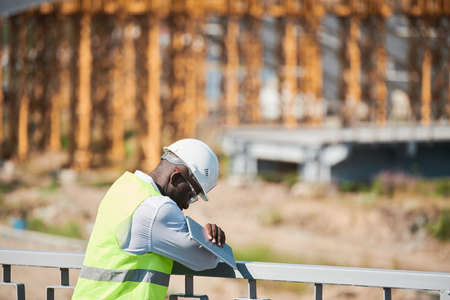 Head and shoulders portrait of bearded construction foreman speaking by walkie-talkie giving instructions to workers on siteの写真素材