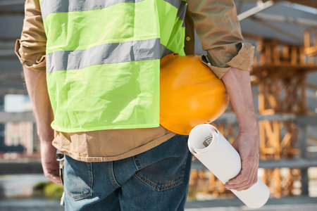 Unknown construction workers holding blueprint and hardhats walking across site outdoors, copy space