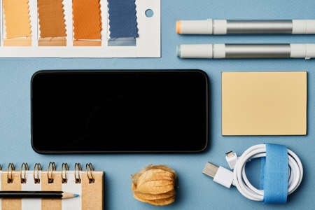 Designers tools such as fabric samlles, charging cord, felt pens, sticky notes, smartphone on blue backgroundの写真素材