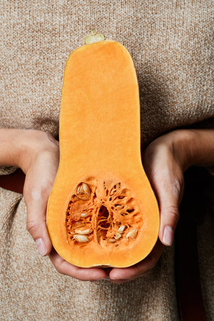 Close-up of unrecognizable woman in beige sweater holding pumpkin part with seeds
