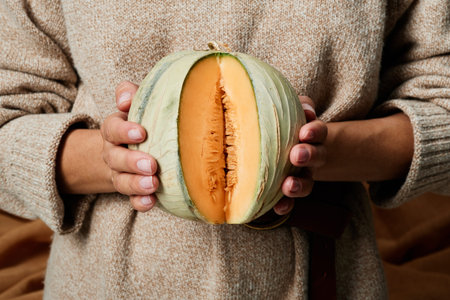 Close-up of unrecognizable woman in warm sweater holding green pumpkin with cut off slice