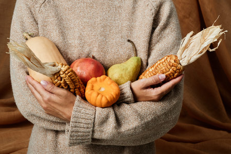 Close-up of unrecognizable woman in sweater holding plenty of fruits and vegetables, autumn concept