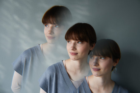 Repetitive exposure of dreamy young Caucasian woman with short hair standing against gray wall