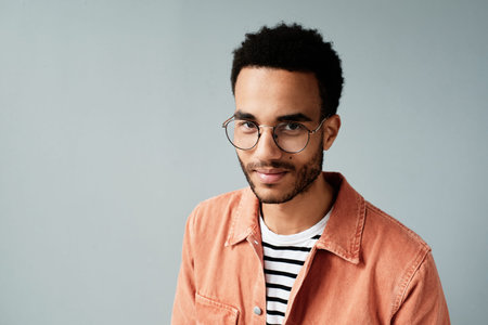 Portrait of smiling handsome young Afro American man in round glasses and casual shirt standing...