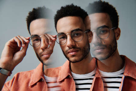 portrait of serious smart African American man with beard adjusting eyewear, repetitive exposureの写真素材