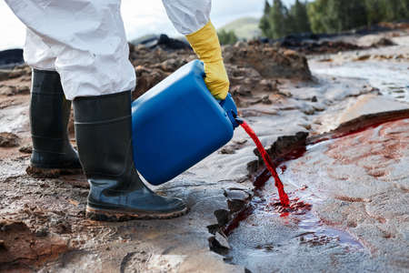 Close-up of unrecognizable ecologist in rubber gloves and boots pouring red toxic liquid into polluted waterの写真素材