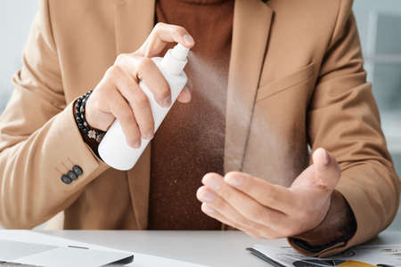 Close-up of unrecognizable office worker in jacket cleaning hands with antiseptic at workplaceの写真素材