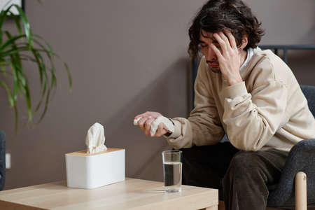 Horizontal medium portrait of young Caucasian man suffering depression having psychologist appointment sitting with eyes closed and cryingの写真素材