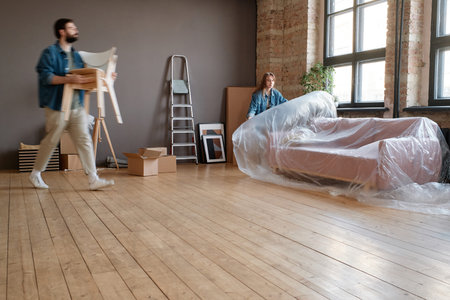 Horizontal long shot of young man and woman getting ready to move to new house packing things and...
