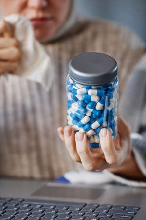 Vertical selective focus close-up shot of mature Caucasian patient sitting at desk in front of laptop showing pills to doctorの写真素材