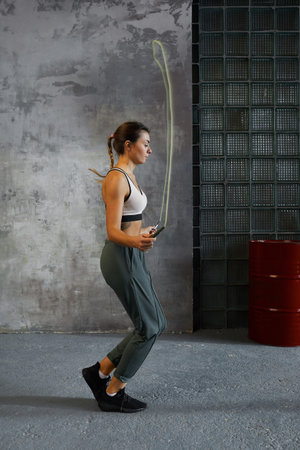 Young woman doing jumping rope warming up exercise before boxing match vertical side view shot