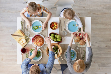 Top view of parents and kids sitting at kitchen table and having tasty lunch together: fresh...