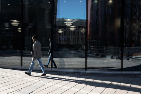 Young Afro-American going along sidewalk past modern office building with glass facade in the...
