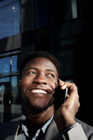 Portrait of African American businessman talking on the phone and smiling happily against office...