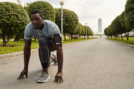 Sprinter getting ready for start. Determined athletic Black man with smartphone in armband standing...