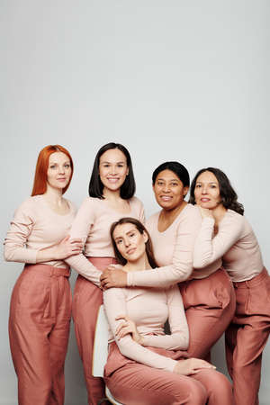 Group of cheerful multi-ethnic women having close connection embracing each other against white wallの写真素材