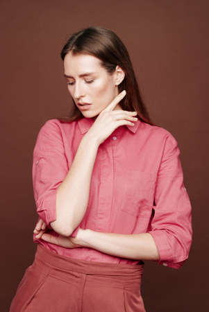 Vulnerable young woman in dark pink blouse demonstrating her weakness while posing against isolated backgroundの写真素材