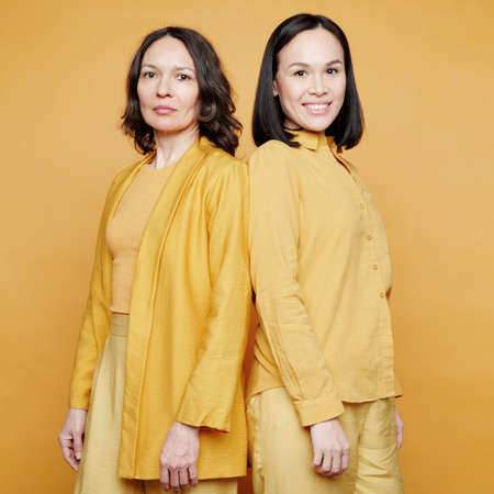 Portrait of serious and smiling multi-ethnic women in yellow clothes standing back to back, womens generation conceptの写真素材