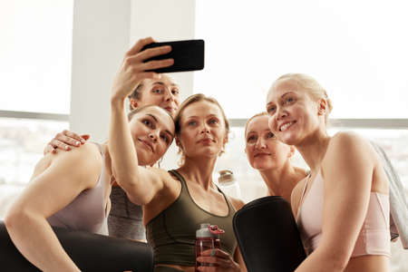 Young teacher using smartphone while photographing with yoga students after yoga classの写真素材