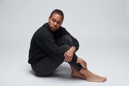 Dejected young Black woman having fear sitting on floor and embracing knees, black lives matter conceptの写真素材