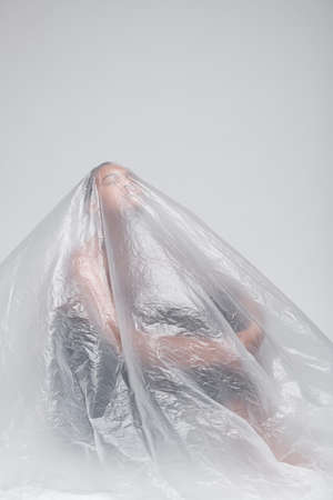 Sad young black woman raising head up while sitting on floor under polyethylene, isolation conceptの写真素材
