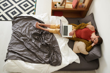 High angle view of young woman sleeping with laptop on bed while resting at home