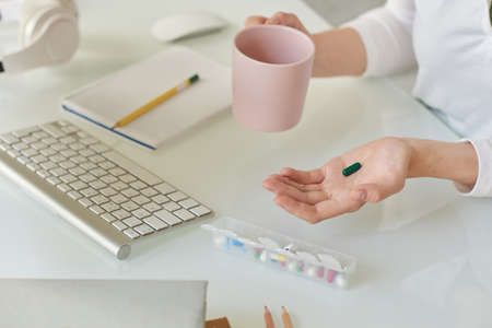 Close-up of unrecognizable manager sitting at table and drinking water while taking vitamin to increase brain function, biohacking conceptの写真素材