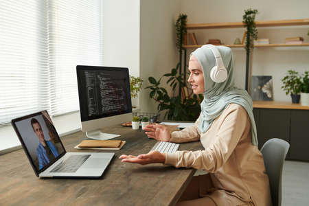 Remote IT specialist wearing headphones discussing new software development problems with her colleagueの写真素材