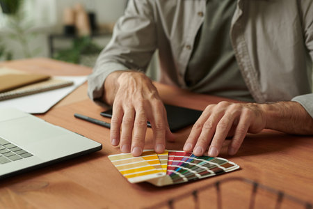 Close-up of unrecognizable web designer sitting at wooden table and choosing palette for design