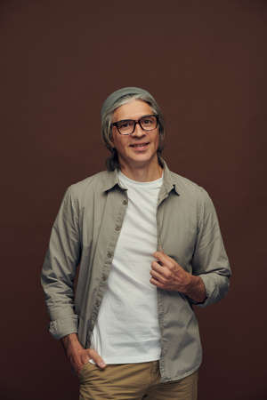 Portrait of serious good-looking mature man with gray hair wearing hipster hat against brown backgroundの写真素材