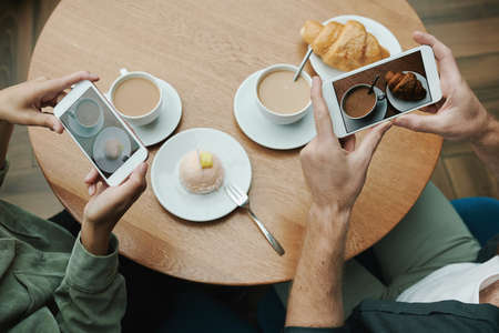 Above view of unrecognizable man and woman taking photo of food on table in cafe, bloggers lifestyle conceptの写真素材