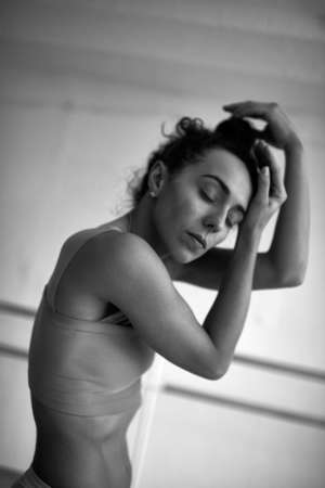 Black and white portrait of young beautiful female dancer making hair bun with her eyes closedの写真素材