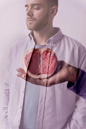 Conceptual portrait of handsome bearded man with closed eyes and female hand holding cut grapefruit...