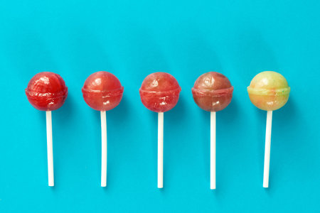 Directly above view of five appetizing lollipops lying in a line against turquoise background