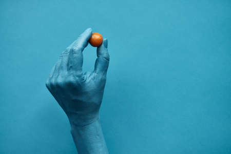 Close-up shot of male hand painted in blue holding ripe cape gooseberry with fingertips against turquoise backgroundの写真素材