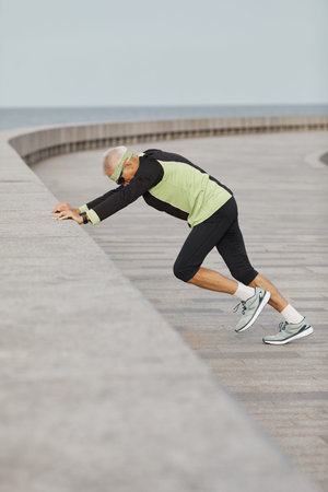 Vertical shot of active unrecognizable elderly man practising aerobic exercise outdoors