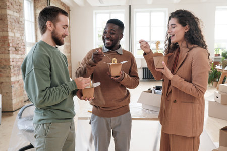 Group of positive young interracial startup company owners standing in circle and chatting while...